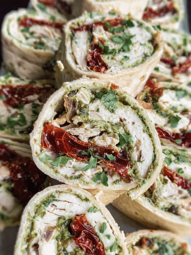 Pesto Chicken Pinwheels sliced on a platter with sun-dried tomatoes and basil.