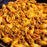 Cheesy taco pasta bake in skillet with melted cheddar and pasta shells
