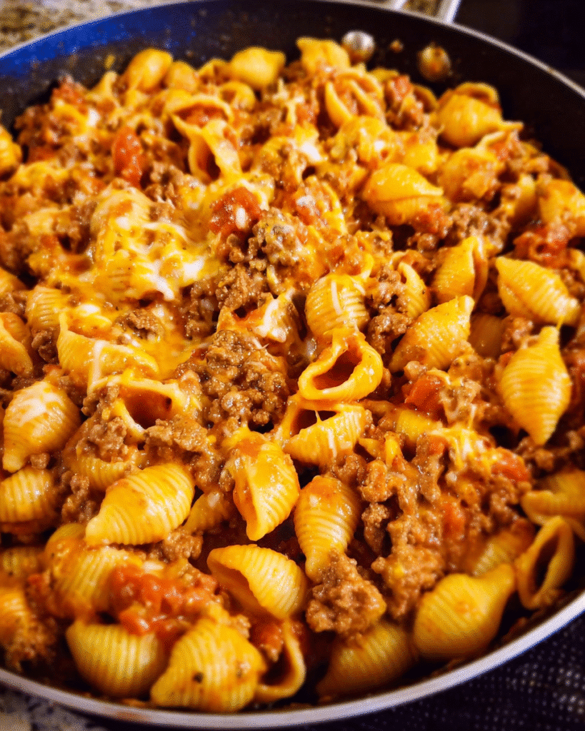 Cheesy taco pasta bake in skillet with melted cheddar and pasta shells