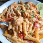 Chicken fajita pasta skillet with peppers, creamy sauce, and lime wedges in a pan