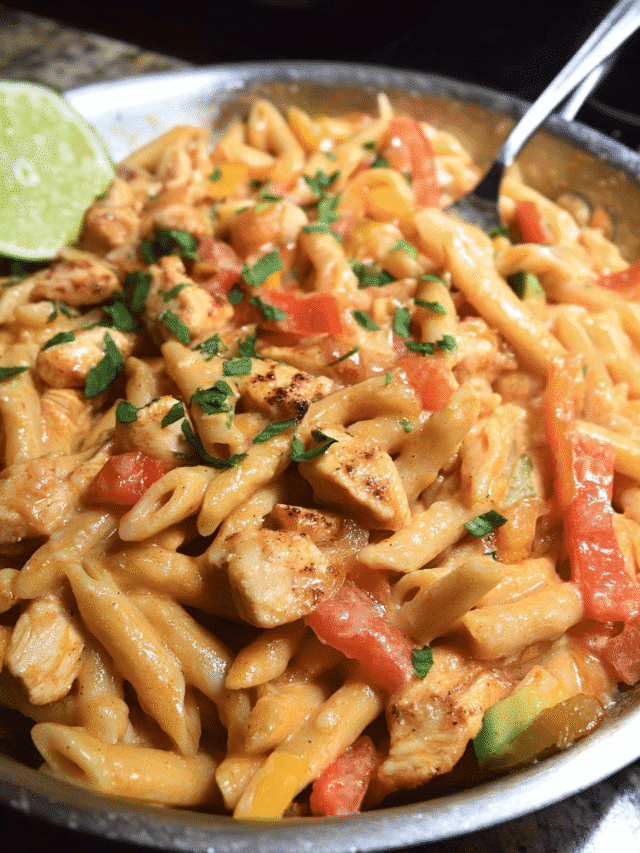 Chicken fajita pasta skillet with peppers, creamy sauce, and lime wedges in a pan