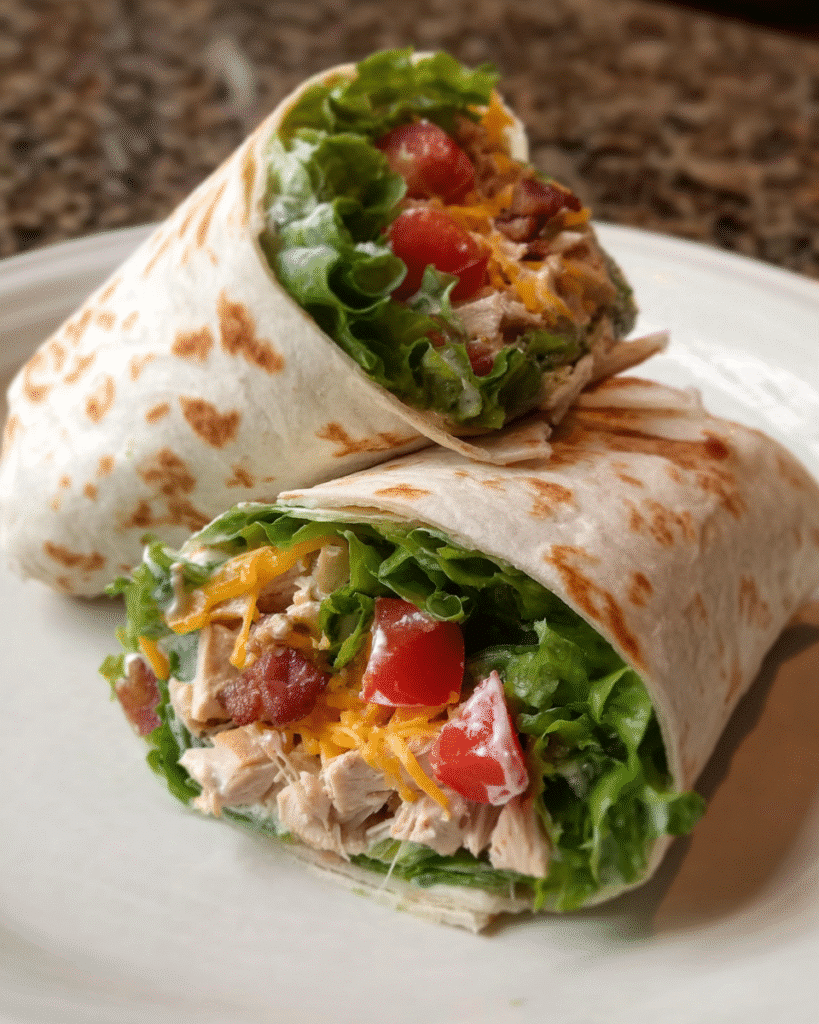 Chicken Bacon Ranch Wrap sliced in half with visible chicken, turkey bacon, cheddar, lettuce, and ranch