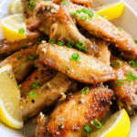 Crispy baked lemon garlic chicken wingettes garnished with lemon wedges and scallions