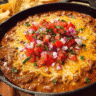 Warm skillet filled with chili cheese dip topped with pico de gallo