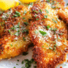 Golden crispy parmesan chicken cutlets served with lemon wedges