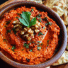 Bowl of roasted red pepper dip with walnuts, olive oil, and parsley served with warm pita bread